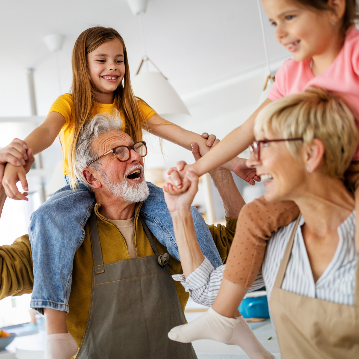 Family of four, including grandparents and two children, holding hands in a circle indoors.